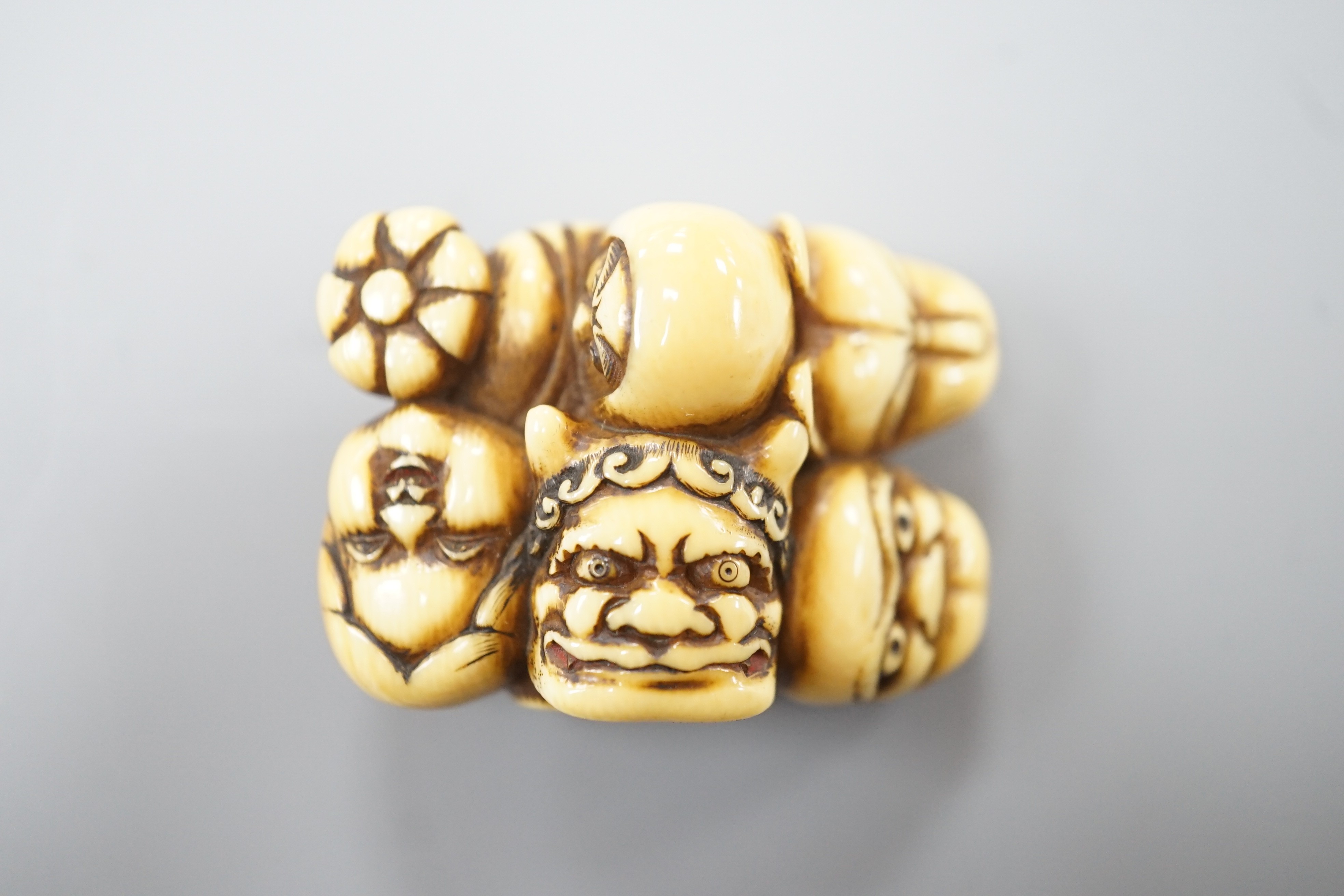 A Japanese ivory netsuke of a Daruma doll and four noh masks, signed, 19th century, 3.8cm